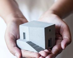 a person holding a small house in their hands with stairs coming out of the building