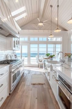 a kitchen with white cabinets and wooden floors next to an ocean front window that overlooks the beach