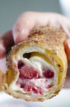 a person holding a pastry with cream and strawberries in it