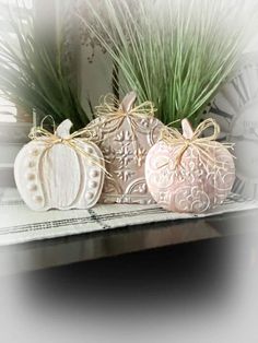 three decorative pumpkins sitting on top of a shelf next to some grass and flowers