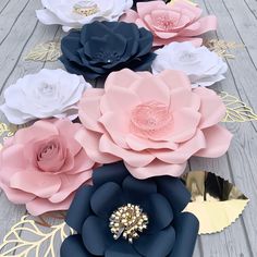 large paper flowers are arranged on a wooden surface with gold leaf accents and blue, pink, and white colors