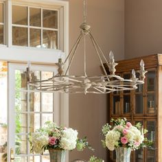 a chandelier hanging over a dining room table with vases and flowers on it