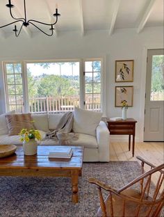 a living room filled with furniture and a wooden table in front of two large windows