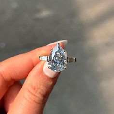 a woman's hand holding an engagement ring with a diamond in the center and two baguettes on each side