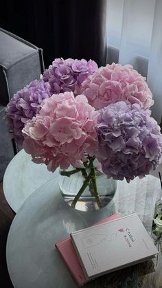 a vase filled with pink and purple flowers on top of a table next to a book