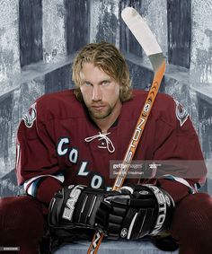 a hockey player sitting in front of a wall with his arms crossed and holding a hockey stick