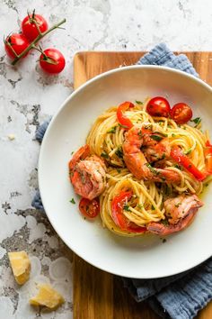 pasta with shrimp and tomatoes in a white bowl on a wooden cutting board next to cherry tomatoes