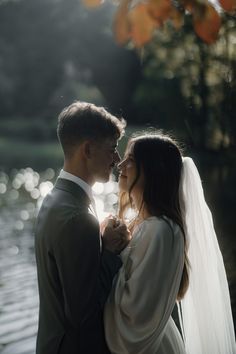 a bride and groom standing next to each other in front of a body of water