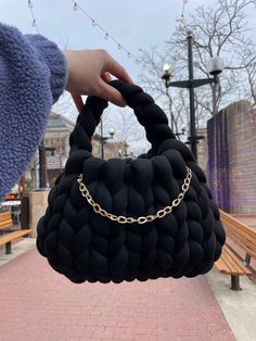 a hand holding a black purse on top of a brick walkway next to a bench