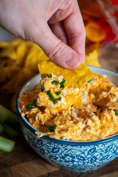 a hand dipping a tortilla chip into a blue and white bowl filled with guacamole