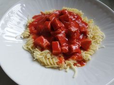 a white plate topped with pasta covered in marinara sauce and diced meat pieces