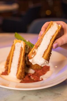 a person is holding up a piece of cake on a white plate with red sauce