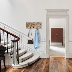 there is a coat rack on the wall next to the stairs in this room with wood floors and white walls