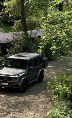 an suv is parked on the side of a dirt road near some trees and bushes