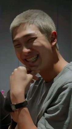 a young man smiling and holding his hand to his face while wearing a watch on his wrist