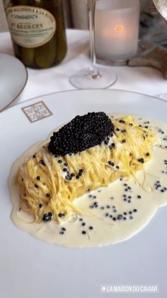 a white plate topped with pasta covered in black cauliflower and sauce next to a glass of wine