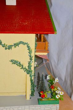 a doll house is shown with flowers in the foreground and an open door on the far side