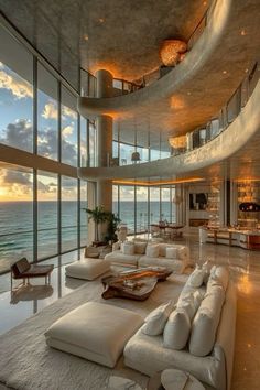 a large living room filled with white furniture next to an ocean front window at sunset