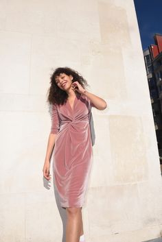 a woman standing in front of a white wall wearing a pink dress and heels with her hand on her hip