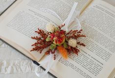 an open book with dried flowers on it and ribbon tied around the top, sitting on a table