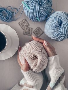 a woman holding a ball of yarn next to two balls of yarn and a cup of coffee