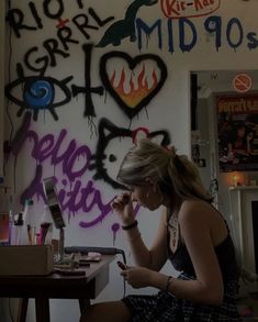 a woman sitting in front of a wall covered in graffiti and writing on her phone