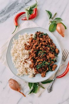 a white plate topped with meat and rice next to red peppers on top of a marble counter