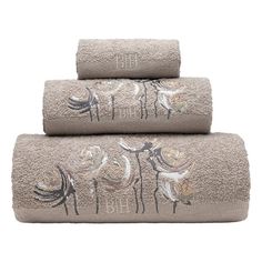 three towels with embroidered animals on them in grey and gold colors, one is folded over the