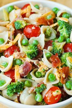 a bowl filled with pasta, peas, tomatoes and broccoli on top of a wooden table