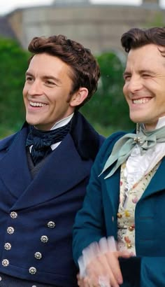 two men dressed in period clothing smile at the camera