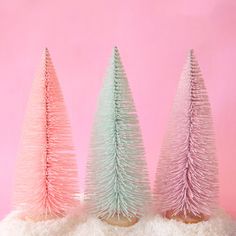 three pink and green christmas trees sitting on top of a pile of white fluffy material