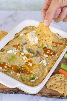 a hand dipping a tortilla chip into a casserole dish with vegetables and crackers