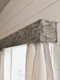 an old window frame is hanging on the side of a white house with sheer curtains