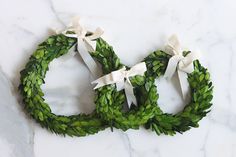 two green wreaths with white bows are on a marble countertop, one is shaped like an oar and the other is made out of leaves