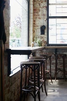 an empty bar with stools in front of the window and brick wall behind it