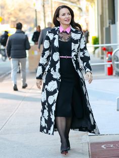 a woman walking down the street wearing a black and white coat with flowers on it