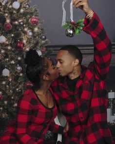 a man and woman kissing in front of a christmas tree with ornaments hanging from it