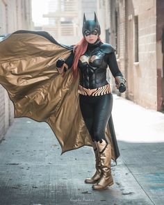 a woman dressed as batgirl is walking down the street with her cape flying in the wind