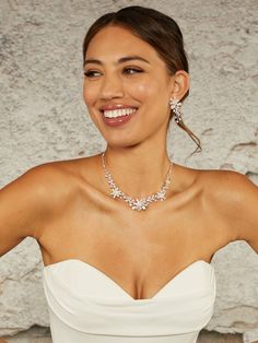 a woman in a strapless white dress smiles at the camera, with her hands on her hips