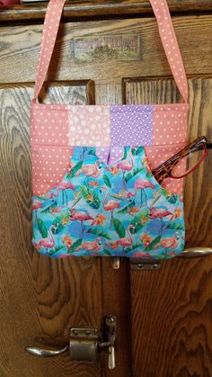 "Carry all your essentials in style with this attractive, fully lined, quilted squares shoulder bag.  The unique design features eight quilted squares & an outside pocket on each side of purse that can easily fit a cell phone.  The purse is held closed by a magnetic snap.  Made with designer cotton fabrics.  The main fabric has cute little flamingos all on a blue background color.  The lining & strap are done in peachy pink/white dot pattern.  The quilted squares are done in coordinating peach & Casual Quilted Square Bags, Casual Quilted Square Shoulder Bag, Quilted Square Travel Bag, Quilted Square Shoulder Bag For Travel, Square Quilted Travel Bag, Pink Rectangular Shoulder Bag With Pockets, Casual Pink Patchwork Bag, Pink Quilted Shoulder Bag For Daily Use, Quilted Rectangular Shoulder Bag For Everyday Use