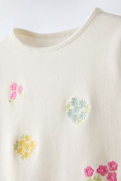 a white sweater with colorful flowers on the front and back buttons in pink, yellow, green, blue, and red