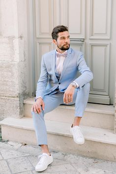 a man in a blue suit and white shoes sitting on steps with his feet up