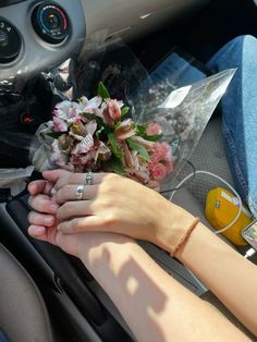 two people holding hands in the back seat of a car with flowers on the dashboard