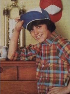 a young man with a hat on top of his head in front of a dresser