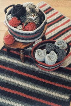 a cat sitting in a basket on top of a rug next to two bowls filled with balls of yarn