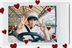 a young man driving a car with hearts around him and holding up the peace sign