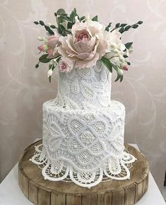 a white wedding cake with pink flowers and greenery on top is sitting on a wooden stand