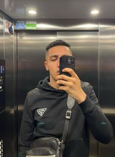 a man taking a selfie in front of an elevator with his cell phone up to his ear