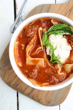 a white bowl filled with pasta and sauce on top of a wooden cutting board next to a spoon