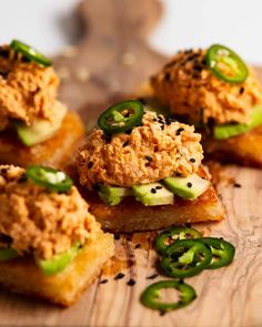 small sandwiches with various toppings sit on a wooden cutting board next to sliced jalapenos